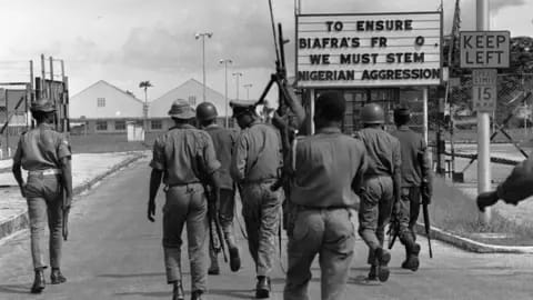 Nigerian soldiers walking toward a checkpoint with a sign about Biafra's freedom